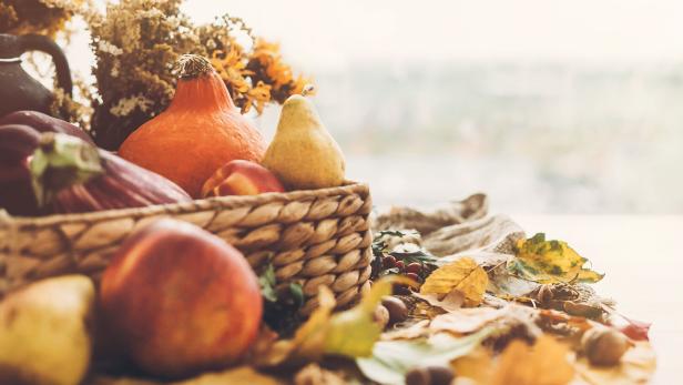 Ein Korb mit Herbstfrüchten und Gemüse, umgeben von bunten Blättern.