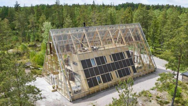 Ein modernes Haus mit Glasfassade und Solarpaneelen inmitten eines Waldes.