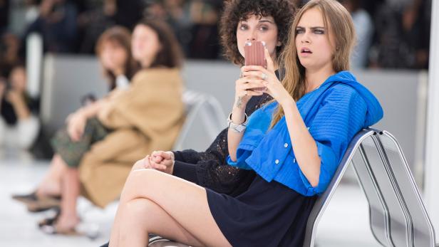 Cara Delevingne sitzt mit einer Freundin zusammen und schaut überrascht.