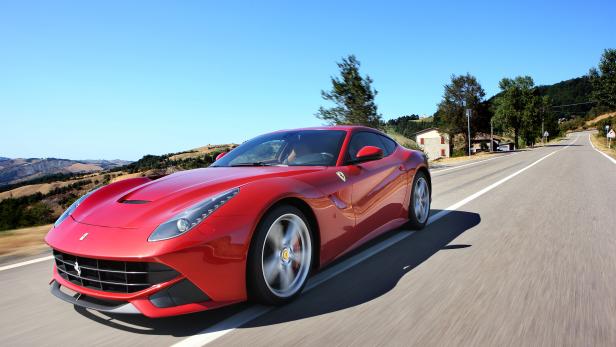 Ein roter Ferrari fährt auf einer Landstraße.