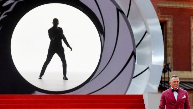 Daniel Craig auf einem roten Teppich vor einer stiliserten Irisblende.
