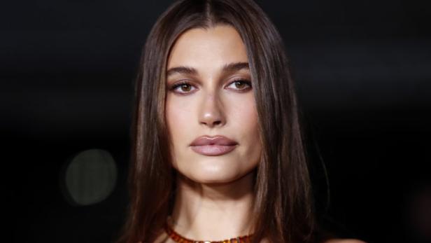 Hailey Bieber trägt ein trägerloses, braunes Kleid und eine bernsteinfarbene Halskette.