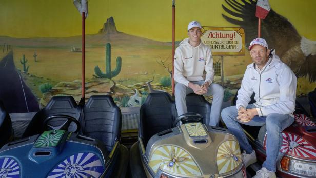 Zwei Männer sitzen auf Autoscootern vor einer Wandmalerei mit Wüstenmotiv.