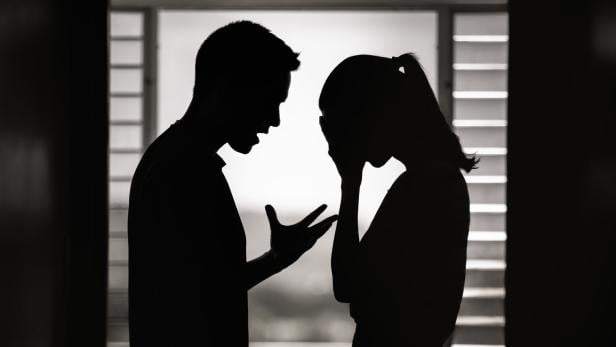 Ein Mann gestikuliert wütend, während eine Frau weinend ihr Gesicht verdeckt.