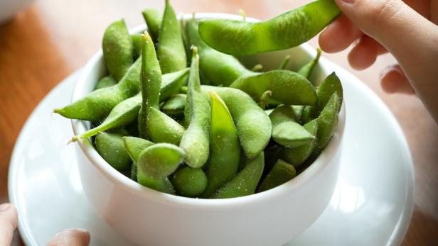 Eine Hand nimmt eine Edamame-Schote aus einer Schüssel.