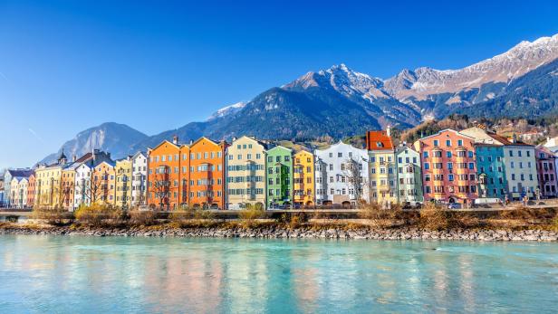 Bunte Häuserzeile am Ufer des Inns in Innsbruck vor einer Bergkulisse.