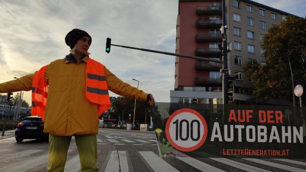 Demonstrierende Frau mit Warnweste hält Plakat in der Hand, auf dem steht "100 auf der Autobahn"