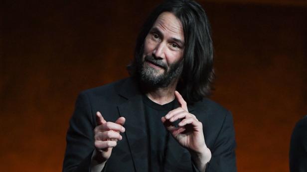 Keanu Reeves gestikuliert während einer Präsentation.