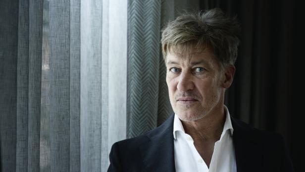 Ein Mann mit blau-grauen Augen und grau meliertem Haar trägt ein weißes Hemd und einen schwarzen Blazer.