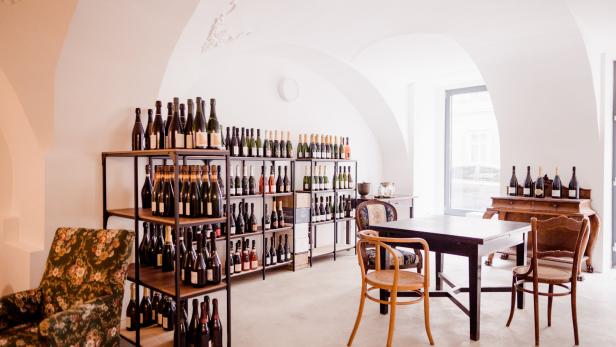 Ein Weinladen mit Regalen voller Weinflaschen und einem Tisch mit Stühlen.