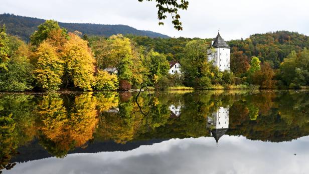 Ein weißes Schloss spiegelt sich in einem ruhigen See, umgeben von Herbstlaub.