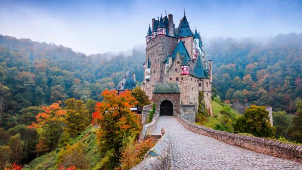 Die Burg Eltz thront auf einem Hügel, umgeben von herbstlichen Wäldern.