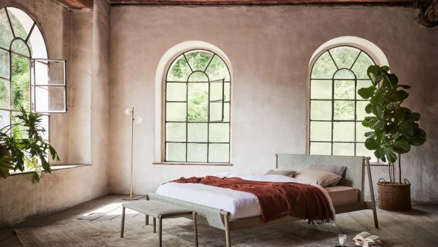 Ein Schlafzimmer mit einem Bett, zwei großen Fenstern und Zimmerpflanzen.