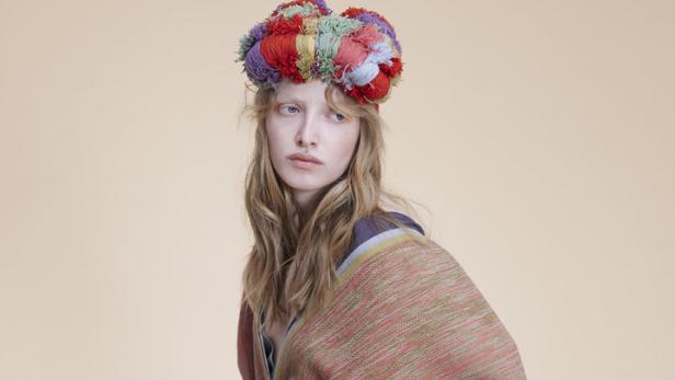Eine Frau mit blonden Haaren trägt einen bunten Kopfschmuck und ein gemustertes Kleid.