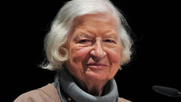 Nahaufnahme einer älteren Frau mit weißen Haaren vor einem schwarzen Hintergrund.