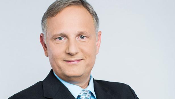 Ein Mann mit Anzug und Krawatte vor einem hellen Hintergrund.