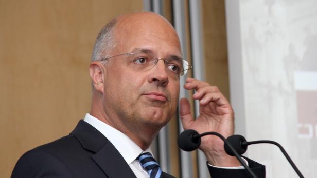 Ein Mann mit Brille und Anzug steht vor einem Mikrofon.