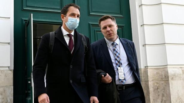 Zwei Männer verlassen ein Gebäude, einer trägt eine Gesichtsmaske.