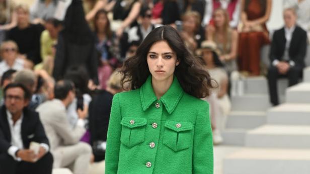 Eine Frau auf dem Laufsteg trägt ein grünes Tweed-Kostüm mit passendem Rock und Stiefeln.