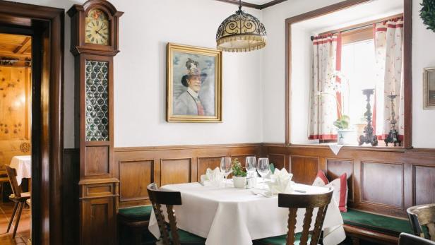 Ein gedeckter Tisch in einem traditionellen bayerischen Restaurant mit einer Standuhr und einem Porträt an der Wand.