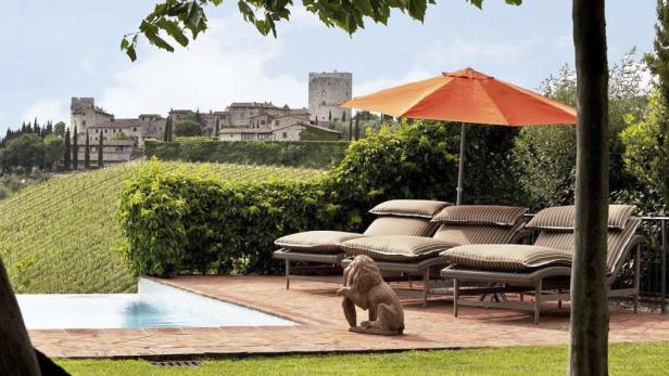 Ein Poolbereich mit Liegestühlen, Sonnenschirm und Blick auf eine toskanische Landschaft mit einem alten Dorf.