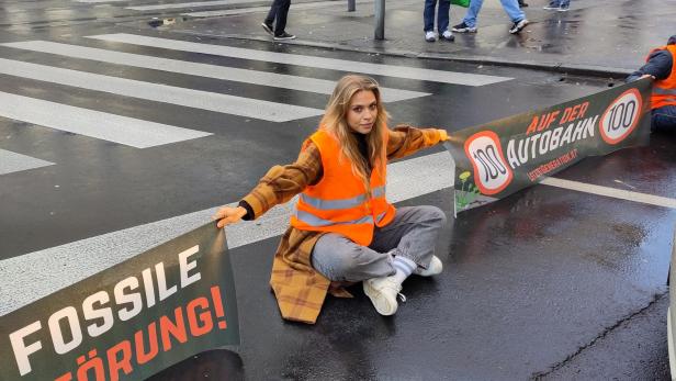 Eine Aktivistin der „Letzten Generation“ blockiert eine Straße mit Bannern gegen fossile Brennstoffe.