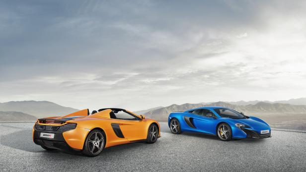 Ein orangefarbener McLaren 650S Spider und ein blauer McLaren 650S stehen vor einer Bergkulisse.