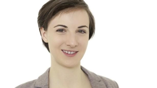 Eine lächelnde junge Frau mit kurzen braunen Haaren und einem Blazer.