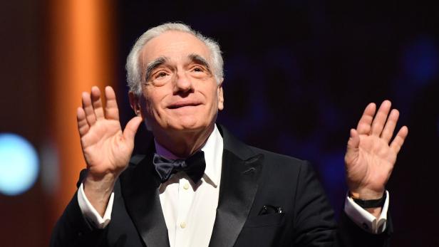 Martin Scorsese in einem Smoking mit Fliege hebt die Hände.