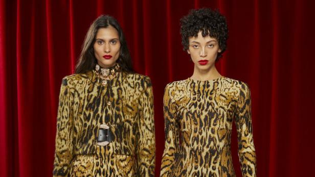 Zwei Models präsentieren Kleidung mit Leopardenmuster vor einem roten Vorhang.
