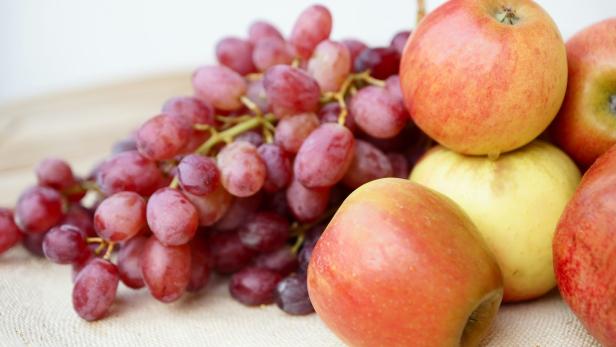 Ein Haufen roter Trauben und mehrere Äpfel liegen auf einem Tisch.