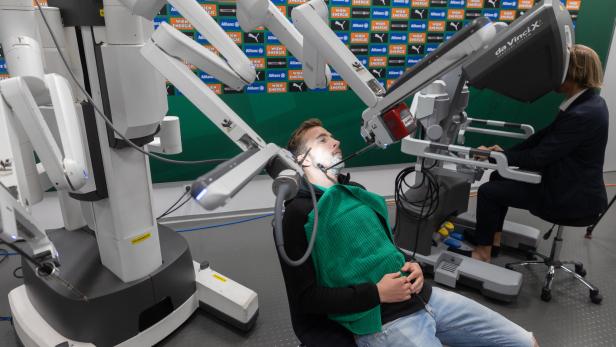 Urologe Oberarzt Michael Lamche steuert den Roboterarm, der Rapid-Kapitän Christopher Dibon rasiert.