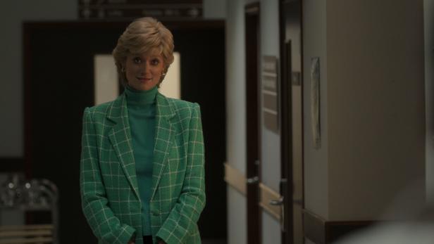 Eine Frau mit blonden Haaren und grünem Blazer steht in einem Flur.