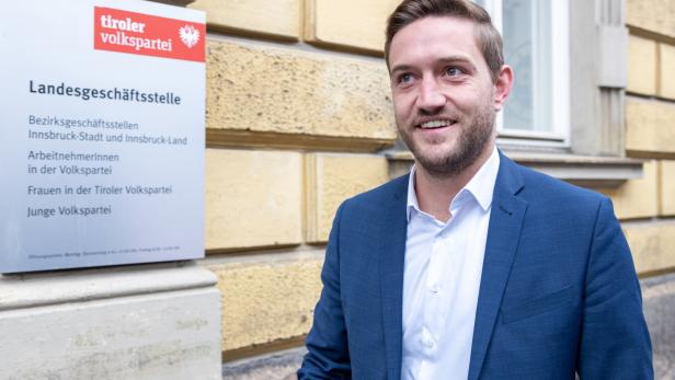Ein lächelnder Mann in einem blauen Anzug steht vor der Landesgeschäftsstelle der Tiroler Volkspartei.
