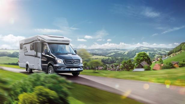 Ein Hymer-Wohnmobil fährt auf einer Landstraße durch eine grüne Landschaft.