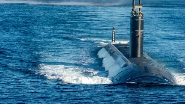 Ein U-Boot fährt auf dem Meer, im Hintergrund ein Flugzeugträger und ein Hubschrauber.