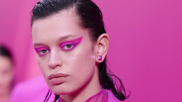 Ein Model mit pinkfarbenem Blazer und auffälligem, pinkfarbenem Augen-Make-up vor pinkfarbenem Hintergrund.