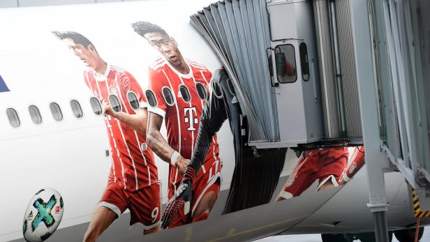 Ein Flugzeug mit einer Werbung des FC Bayern München am Rumpf steht an einem Flugsteig.