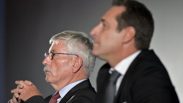 Zwei Männer in Anzügen sitzen nebeneinander und schauen in die Ferne.