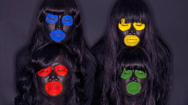 Vier Frauen mit schwarzer Farbe im Gesicht und farbigen Akzenten um Augen und Lippen posieren.