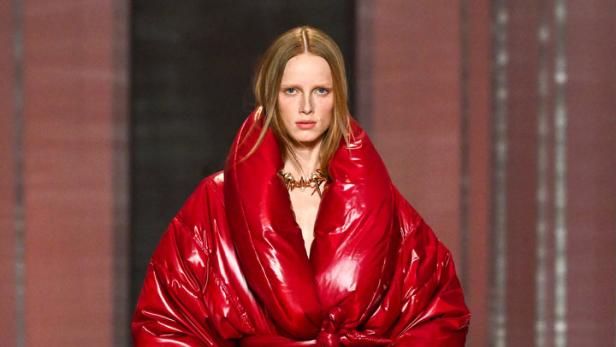 Ein Model präsentiert einen glänzenden, roten Daunenmantel mit passenden Stiefeln auf dem Laufsteg.