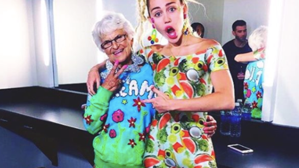 Miley Cyrus posiert mit einer älteren Frau in farbenfrohen Kleidern.