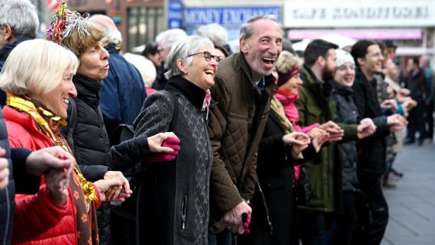 Eine Menschengruppe hält Hände und bildet eine Kette in einer Stadt.