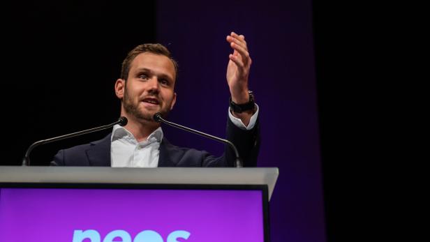 Ein Mann hält eine Rede vor einem „neos“-Logo.