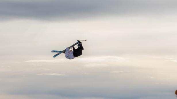 Ein Skifahrer springt über eine Rampe vor einer Bergkulisse.