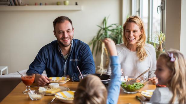 Eine Familie sitzt lächelnd beim Mittagessen am Tisch.