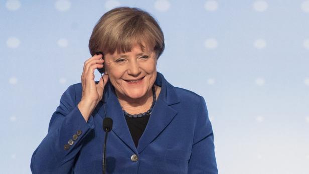 Angela Merkel lächelt und trägt ein blaues Jackett und ein Headset.