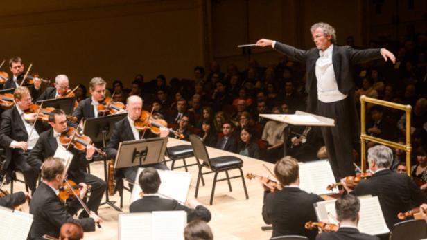 Ein Orchester spielt unter der Leitung eines Dirigenten vor einem Publikum.