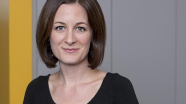 Eine Frau mit braunen Haaren und einem schwarzen Oberteil lächelt in die Kamera.