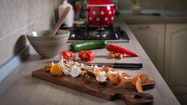 Gemüsereste liegen auf einem Schneidebrett in einer Küche.